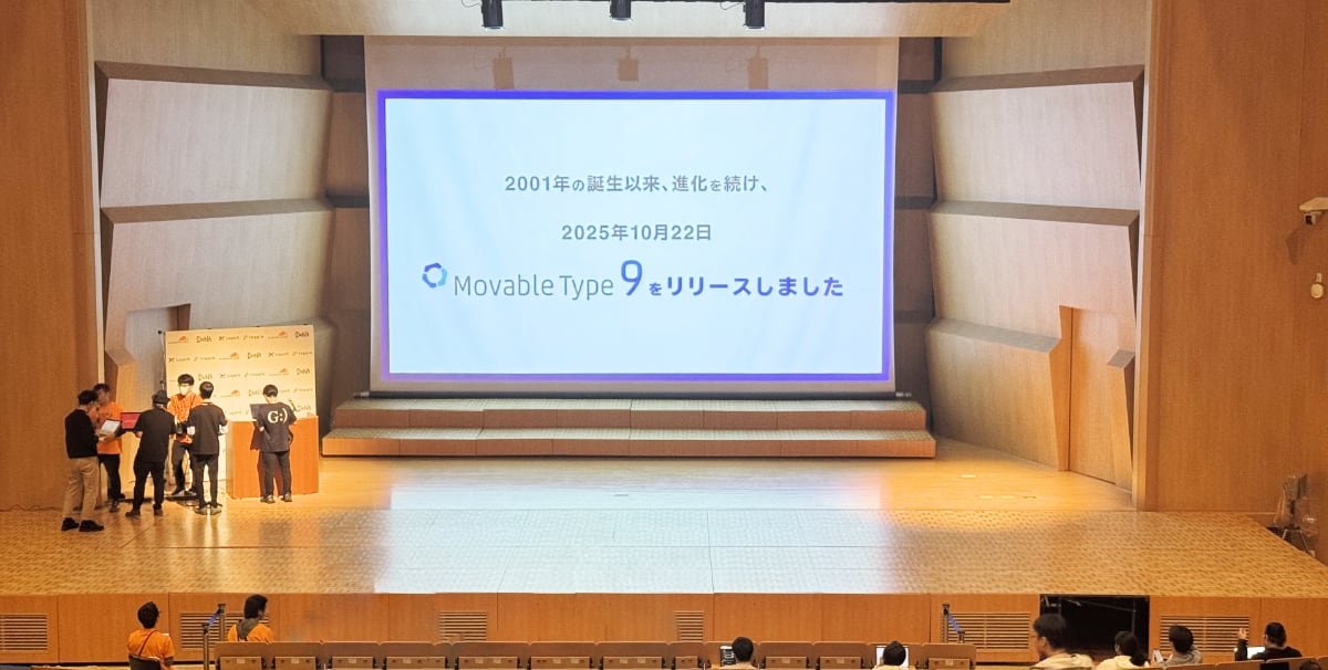 YAPC::Fukuoka セッション会場となった大講堂のスクリーンに「2001年の誕生以来進化を続け、2025年10月22日　Movable Type 9 をリリースしました」と書かれたCM動画のワンシーンが表示されている写真
