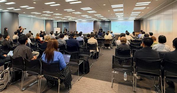 多くの参加者が着席する会場後方から見た、早瀬の登壇の様子。前方のスクリーンにセッションのタイトルスライドが投影されている